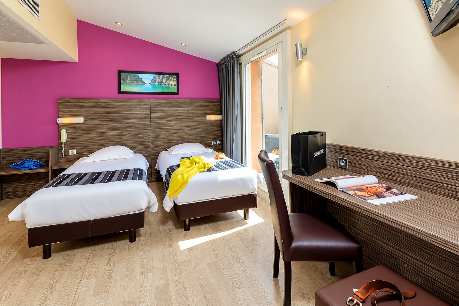 Chambre d'hôtel avec deux lits simples, un mur fuchsia et une porte-fenêtre sur balcon