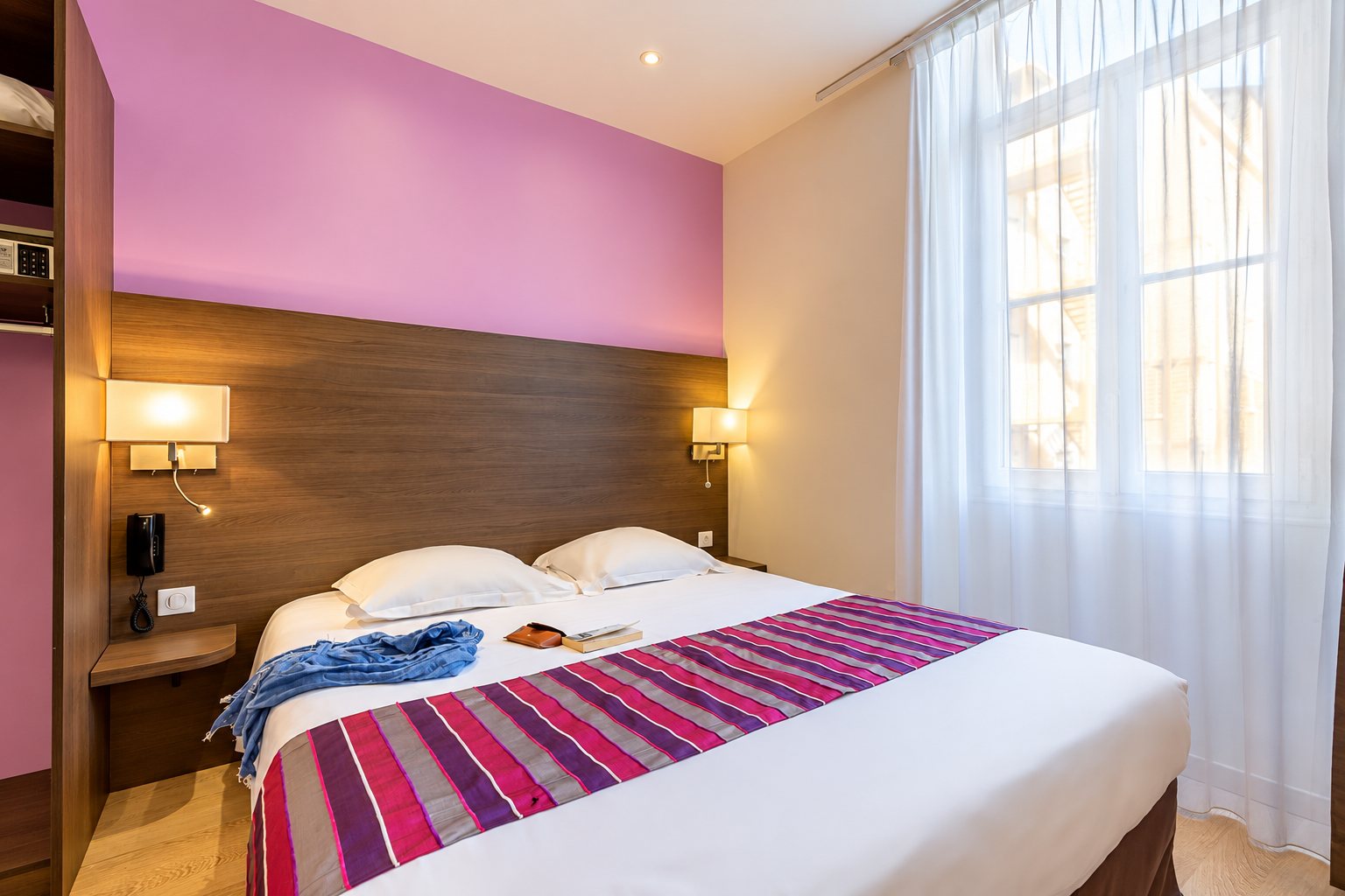 Chambre d'hôtel avec un lit double, un mur rose et de grands rideaux blancs