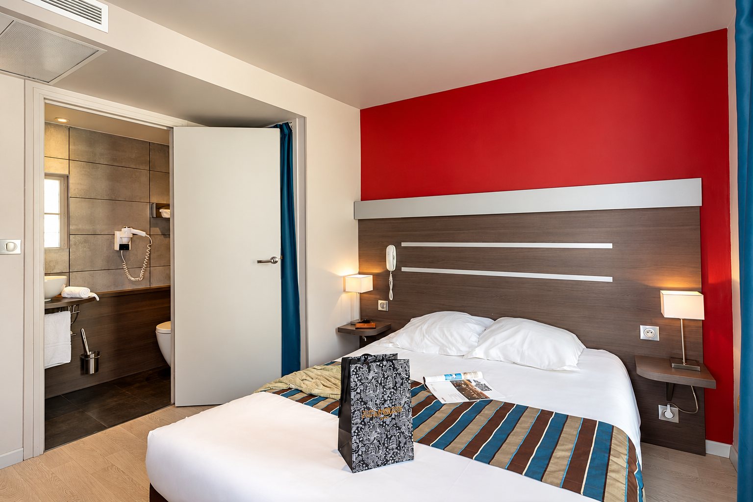 Chambre d'hôtel avec un lit double, un mur rouge et la salle de bain ouverte sur la gauche