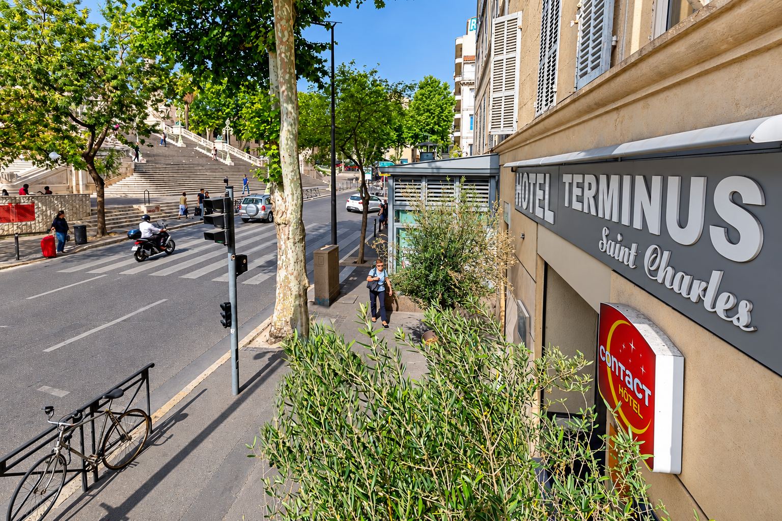 Enseigne de l'hôtel Terminus Saint-Charles sur la façade, avec la rue et le grand escalier en arrière-plan
